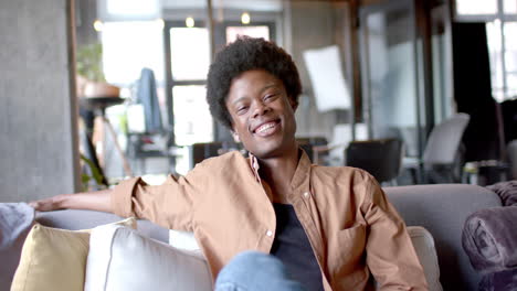 Portrait-of-happy-african-american-man-with-afro-sitting-on-sofa-at-home,-slow-motion