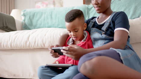 African-american-sister-and-brother-using-tablet-and-smartphone-in-living-room,-slow-motion