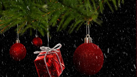 Animation-Von-Schnee,-Der-über-Hängende-Kugeln-Und-Weihnachtsgeschenke-Auf-Einem-Ast-Auf-Schwarzem-Hintergrund-Fällt