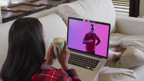 Biracial-woman-watching-laptop-with-african-american-male-rugby-player-catching-ball-on-screen