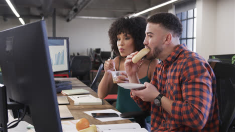 Happy-diverse-male-and-female-colleagues-eating-at-desk-and-watching-computer-in-office,-slow-motion