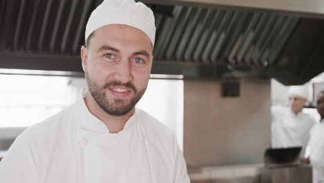 Portrait-of-happy-bearded-caucasian-male-chef-in-hat-smiling-in-kitchen,-copy-space,-slow-motion