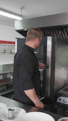 Caucasian-male-chef-closing-oven-doors-and-crossing-arms-in-kitchen,-slow-motion,-vertical