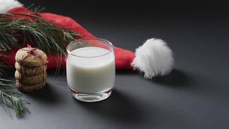 Video-of-christma-cookies,-glass-of-miljk,-santa-clasus-hat-and-copy-space-on-black-background