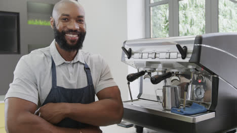 Portrait-of-happy-african-american-male-barista-with-arms-crossed-smiling-in-cafe,-in-slow-motion