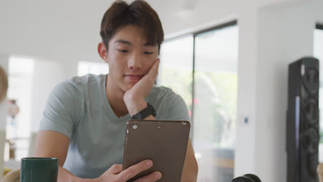 Gelangweilter-Asiatischer-Männlicher-Teenager,-Der-Tablet-Benutzt-Und-Im-Wohnzimmer-Sitzt