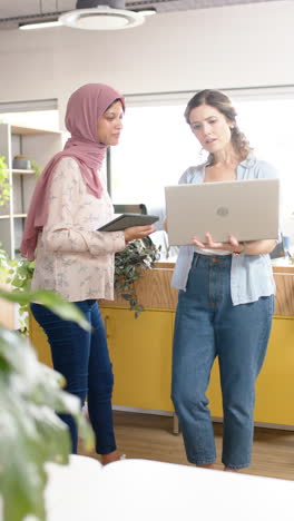 Vertical-video-of-diverse-female-creative-colleagues-discussing-using-laptop-in-office,-slow-motion