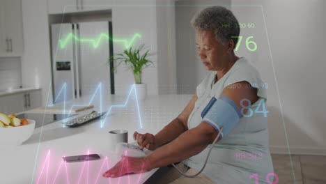 Animation-of-heart-rate-monitor-over-african-american-senior-woman-checking-blood-pressure-at-home