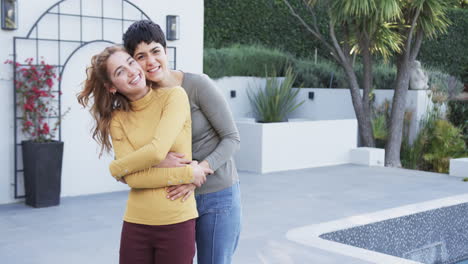 Happy-caucasian-lesbian-couple-standing,-embracing-and-smiling-in-front-of-house