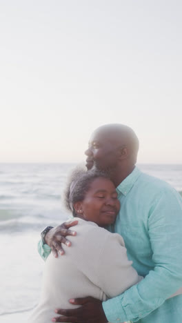 Vertical-video-of-senior-african-american-couple-embracing-at-beach,-in-slow-motion