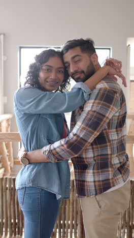 Vertical-video-of-portrait-of-happy-biracial-couple-embracing-and-smiling-at-home,-slow-motion