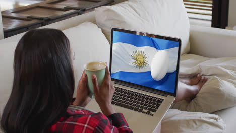 Biracial-woman-watching-laptop-with-rugby-ball-on-flag-of-argentina-on-screen