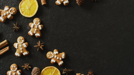 Video-of-smiling-gingerbread-men-and-spices,-slices-of-orange-and-nuts-over-black-background