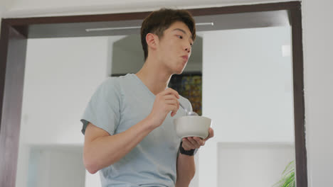Asian-male-teenager-looking-away-and-having-breakfast-in-living-room