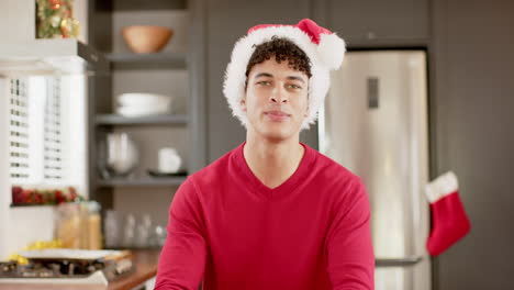 Biracial-man-wearing-christmas-hat-on-video-call-in-kitchen-at-home,-slow-motion,-copy-space