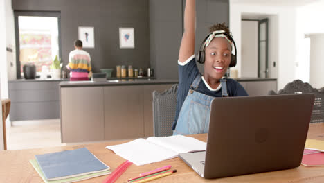 Fröhliches-Afroamerikanisches-Mädchen-Mit-Kopfhörern-Und-Laptop,-Das-Im-Online-Unterricht-Die-Hand-Hebt,-Langsame-Bewegung