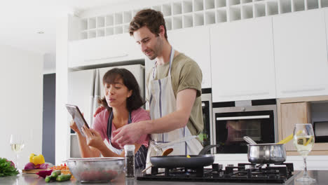 Video-of-happy-diverse-couple-preparing-meal-together-with-tablet