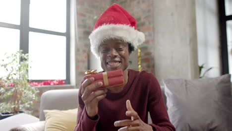 Glücklicher-Afroamerikanischer-Mann-Mit-Weihnachtsmütze,-Der-Auf-Dem-Sofa-Sitzt-Und-Zu-Hause-Einen-Videoanruf-Macht,-Zeitlupe