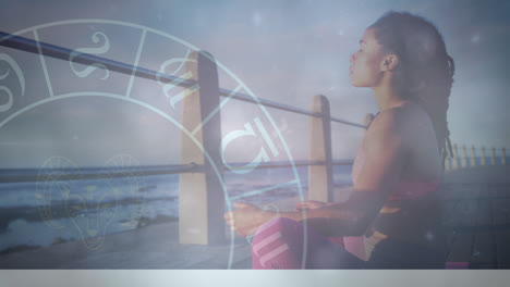 Animation-of-zodiac-signs-with-young-african-woman-meditating-on-pier-at-beach