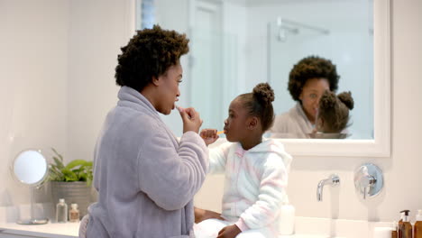 Young-African-American-mother-brushes-teeth-with-African-American-daughter-at-home