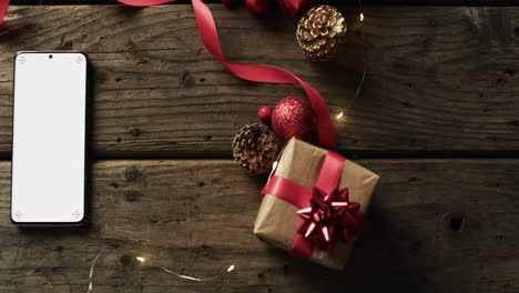 Video-of-christmas-decorations,-present-with-smartphone-and-copy-space-on-wooden-background