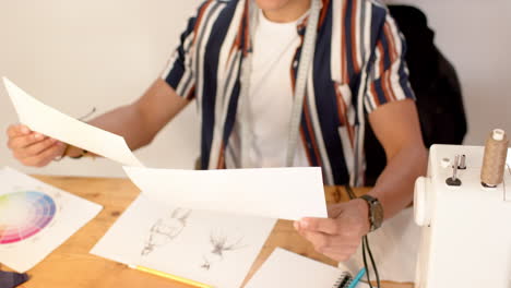 Biracial-male-fashion-designer-looking-at-sketched-designs-in-studio,-slow-motion