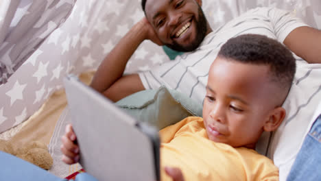 Happy-african-american-father-and-son-using-tablet-and-smiling-at-home,-slow-motion