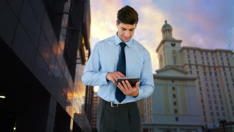 Composite-view-of-biracial-businessman-using-digital-tablet-against-tall-buildings-and-sunset-sky