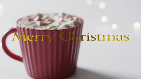 Merry-christmas-text-in-gold-over-hot-chocolate-with-marshmallows-on-grey-background
