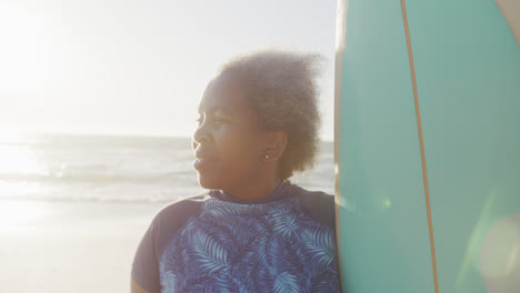 Happy-senior-african-american-woman-holding-surfboard-at-beach,-in-slow-motion