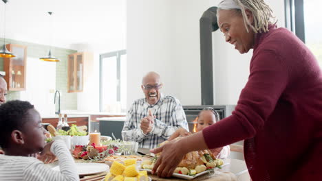 Happy-african-american-multi-generation-family-serving-food-at-thanksgiving-dinner,-slow-motion