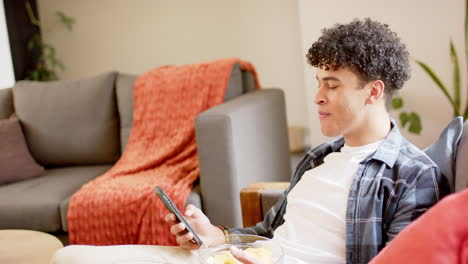Biracial-man-sitting-on-couch-and-using-smartphone,-slow-motion