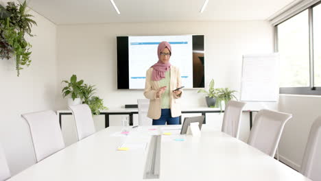 Biracial-casual-businesswoman-in-hijab-talking-on-smartphone-in-meeting-room,-slow-motion