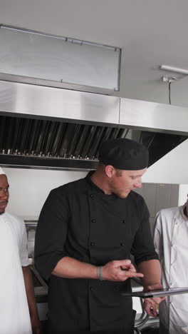 Focused-diverse-male-chef-instructing-trainee-male-chefs-in-kitchen,-slow-motion,-vertical