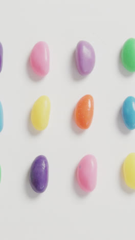Video-of-overhead-view-of-rows-of-multi-coloured-sweets-over-white-background