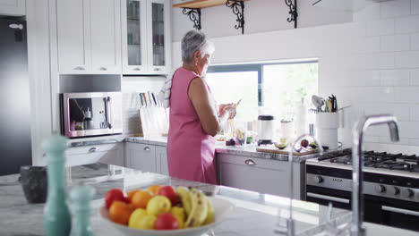 Happy-senior-biracial-woman-preparing-healthy-drink-in-kitchen