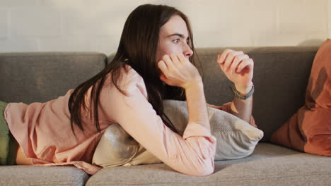 Young-Caucasian-transgender-woman-lounges-on-a-sofa-at-home,-looking-thoughtful