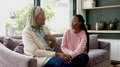 Happy-african-american-senior-mother-and-adult-daughter-sitting-on-couch-and-talking,-slow-motion
