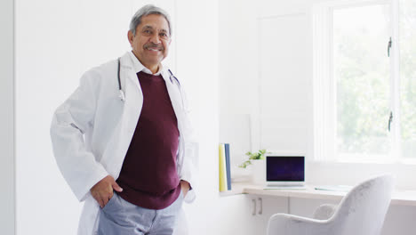 Video-portrait-of-biracial-male-doctor-standing-in-office-with-arms-crossed-smiling-to-camera