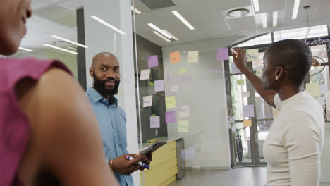 Happy-african-american-colleagues-brainstorming,-making-notes-on-glass-wall-in-office-in-slow-motion