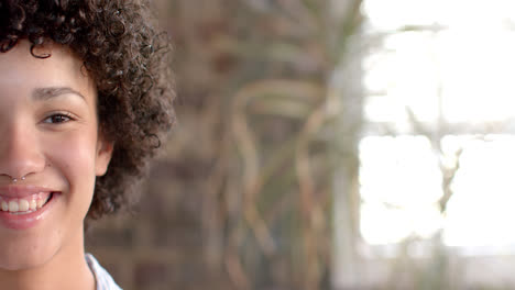 Portrait-of-happy-biracial-casual-businesswoman-with-curly-hair-in-office-in-slow-motion