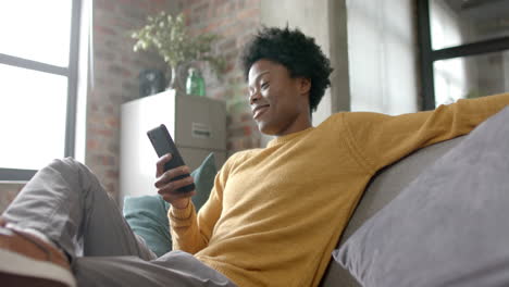 Happy-african-american-man-sitting-on-sofa-using-smartphone-at-home,-slow-motion