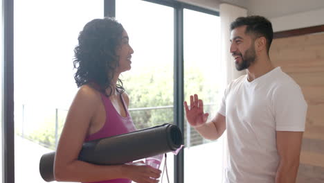 Happy-biracial-couple-holding-yoga-mats-and-highfiving-at-home,-in-slow-motion