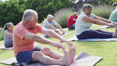 Diverse-group-of-happy-male-and-female-seniors-exercising-in-garden,-touching-toes,-slow-motion