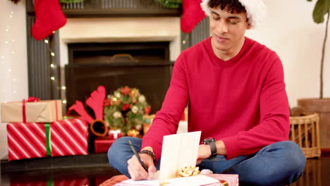 Biracial-man-writing-christmas-greetings-on-christmas-card-at-home,-slow-motion