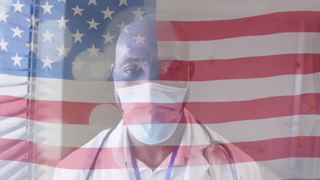 Animation-of-american-flag-and-spots-over-african-american-male-doctor-in-face-mask