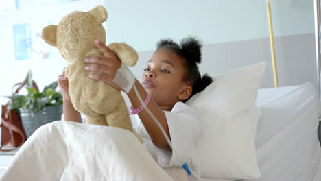 Happy-african-american-girl-playing-with-mascot-in-hospital-bed,-slow-motion