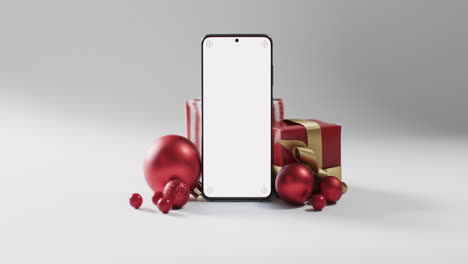 Video-of-christmas-presents,-baubles-and-smartphone-with-copy-space-on-white-background