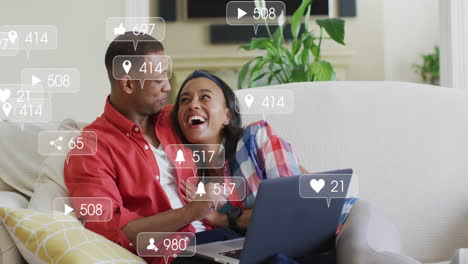 Animation-of-social-media-notifications-over-african-american-couple-using-laptop-embracing-on-couch
