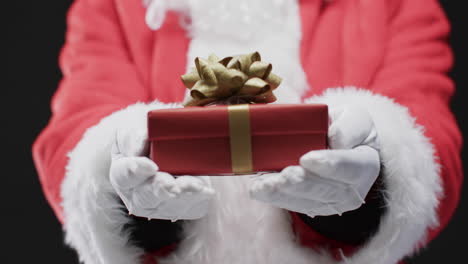 Video-of-santa-claus-holding-christmas-present-with-copy-space-on-black-background